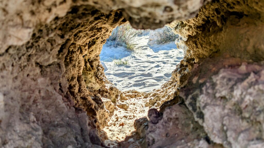 pexels-photo-29340422-29340422 View of a sandy beach through a natural rock formation, capturing erosion effects.