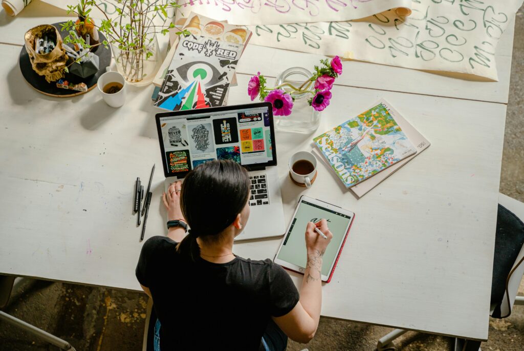 pexels-photo-4348401-4348401 Artistic workspace featuring calligraphy and digital design on a tablet and laptop.